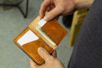 Tan full grain leather minimalist bifold wallet for men and women that holds cash and cards. Held by a person with a blurred background.
